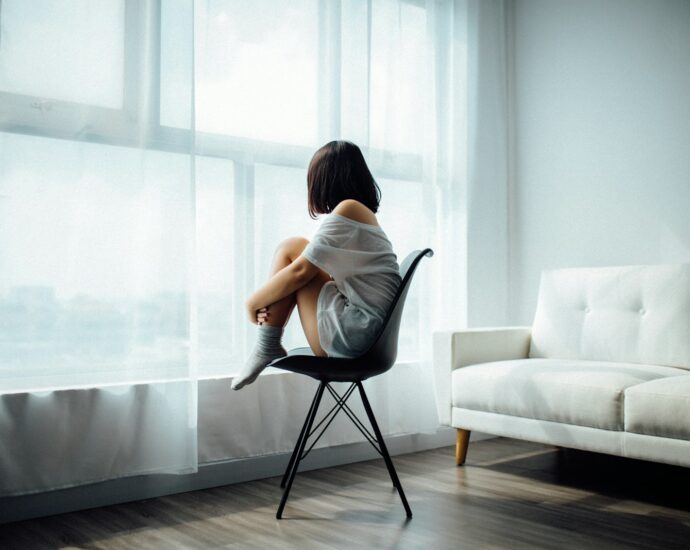 woman sitting on black chair in front of glass-panel window with white curtains